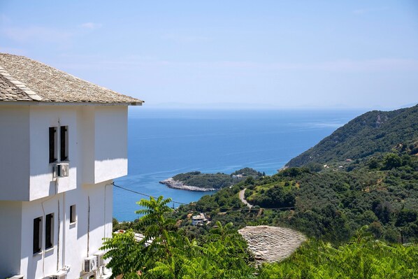 A white building with air conditioning units, overlooking a coastal landscape with a clear view of the sea and a hilly terrain.
