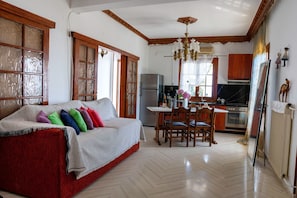 A cozy living room with a red sofa, wooden dining table, and a kitchen area with wooden cabinets and a refrigerator. - Paradeisos Partment With Sea View (Zagora-Mouresi)