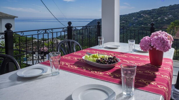 A table set for two with a red tablecloth, a bowl of fruit, and two glasses of water.