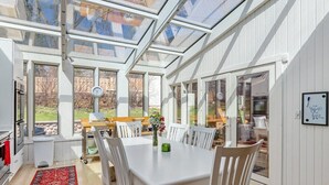 A dining area with a white table and chairs, a red rug, and a glass ceiling. - Timber Ridge-An Artist Retreat Infused w/Character |Perched on a Hill Overlooking Geneva Lake & Town (Lake Geneva)
