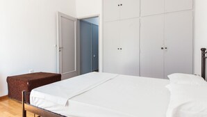 A bedroom with a bed, a brown bench, and a wardrobe with multiple doors. - Brand new 1 Bedroom Apt in Kolonaki (Athens)