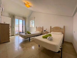 Quarto com duas camas de solteiro, um guarda-roupa de madeira e uma pequena mesa de cabeceira com abajur.
