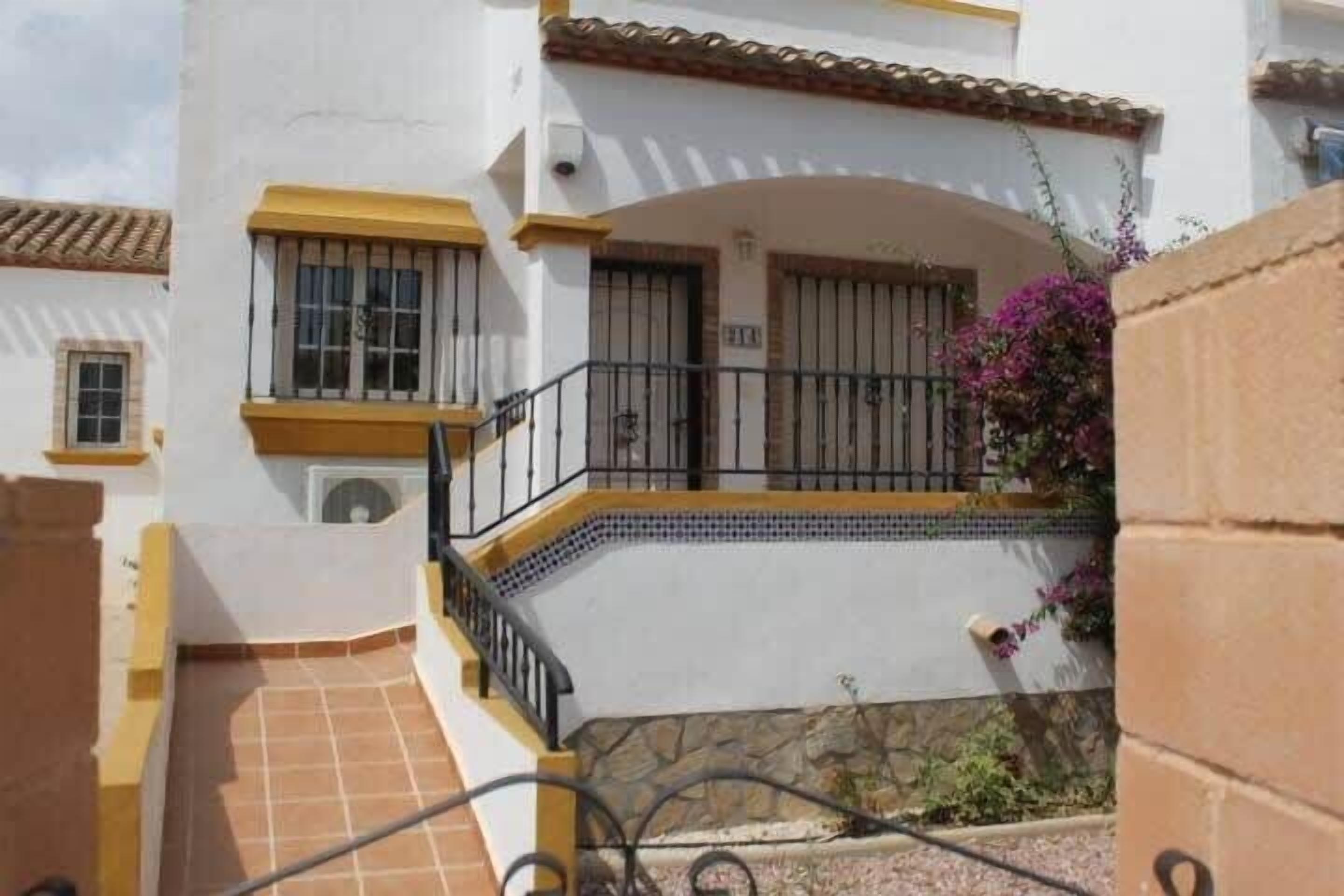 A two-story building with a balcony, a tiled floor, and a small garden area with purple flowers.