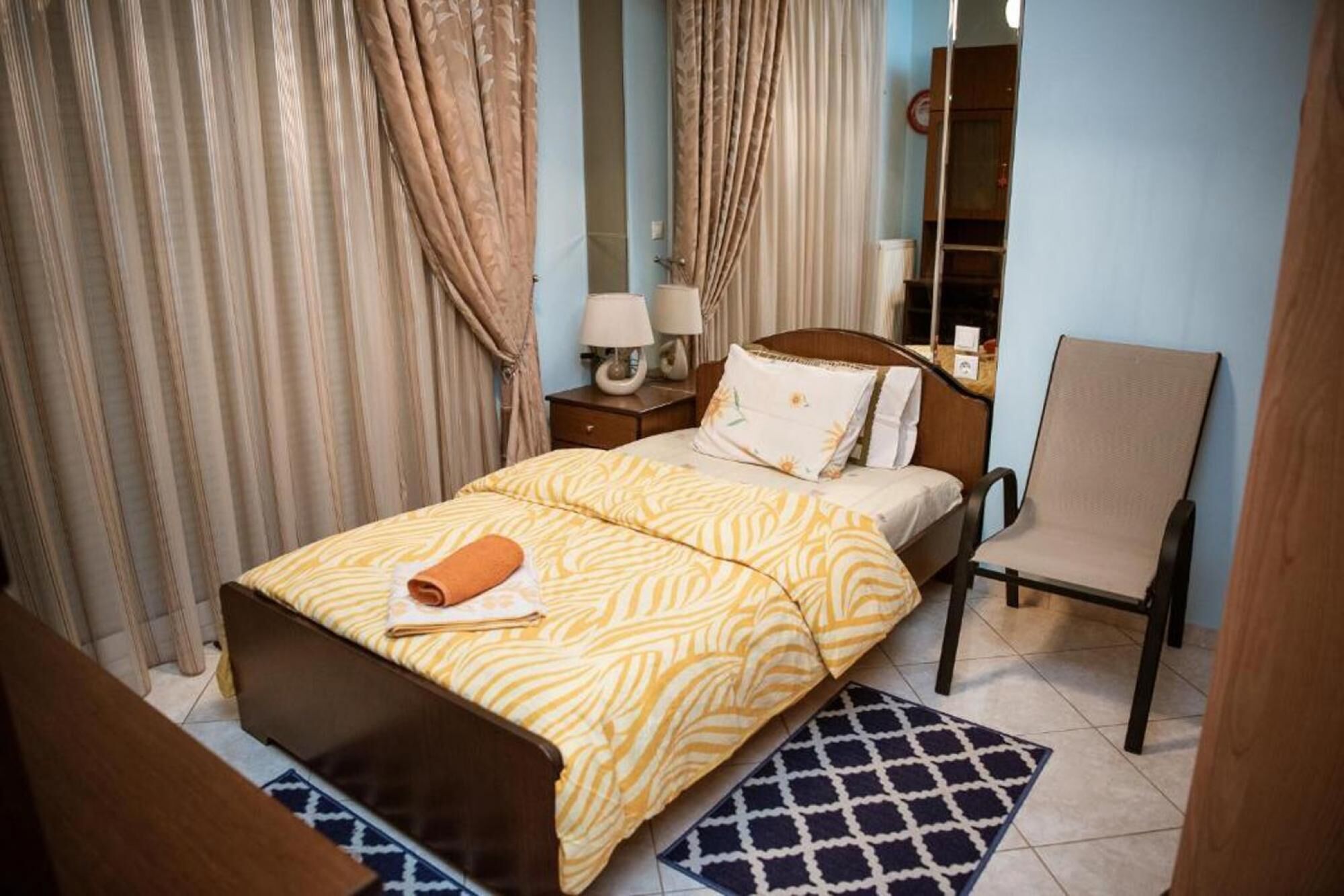 A neatly arranged hotel room with a bed, a chair, a nightstand, and a mirror.