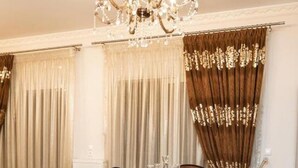 A dining area with a chandelier, curtains, a sofa, and a dining table with chairs.