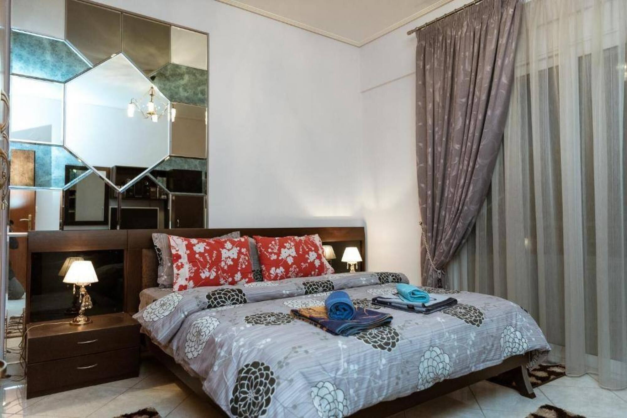 A bedroom with a bed, bedside tables, a mirror, and a window with curtains.