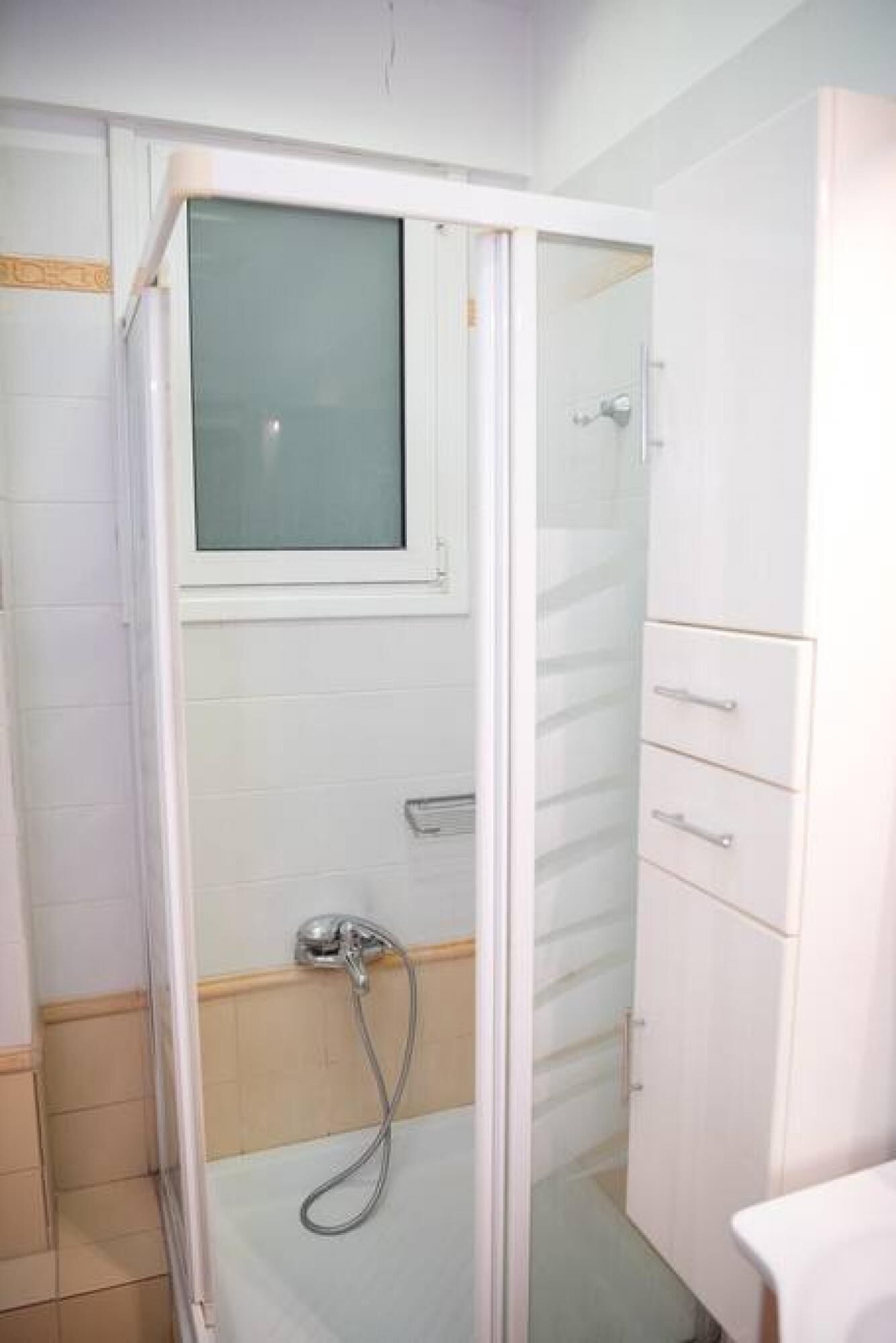 A small, enclosed shower area with a glass door, a showerhead, and a towel rack.