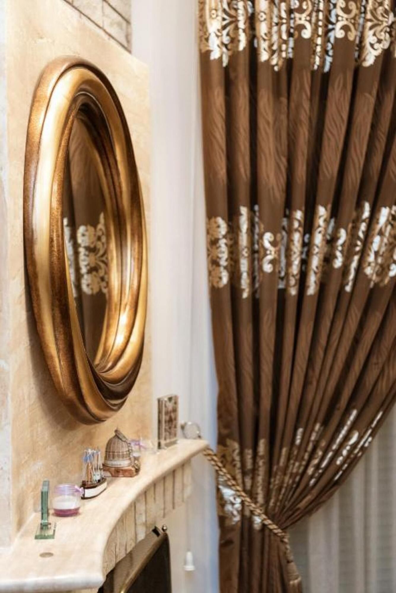 A bathroom with a gold-framed mirror, a marble sink, and a decorative shelf with small items.