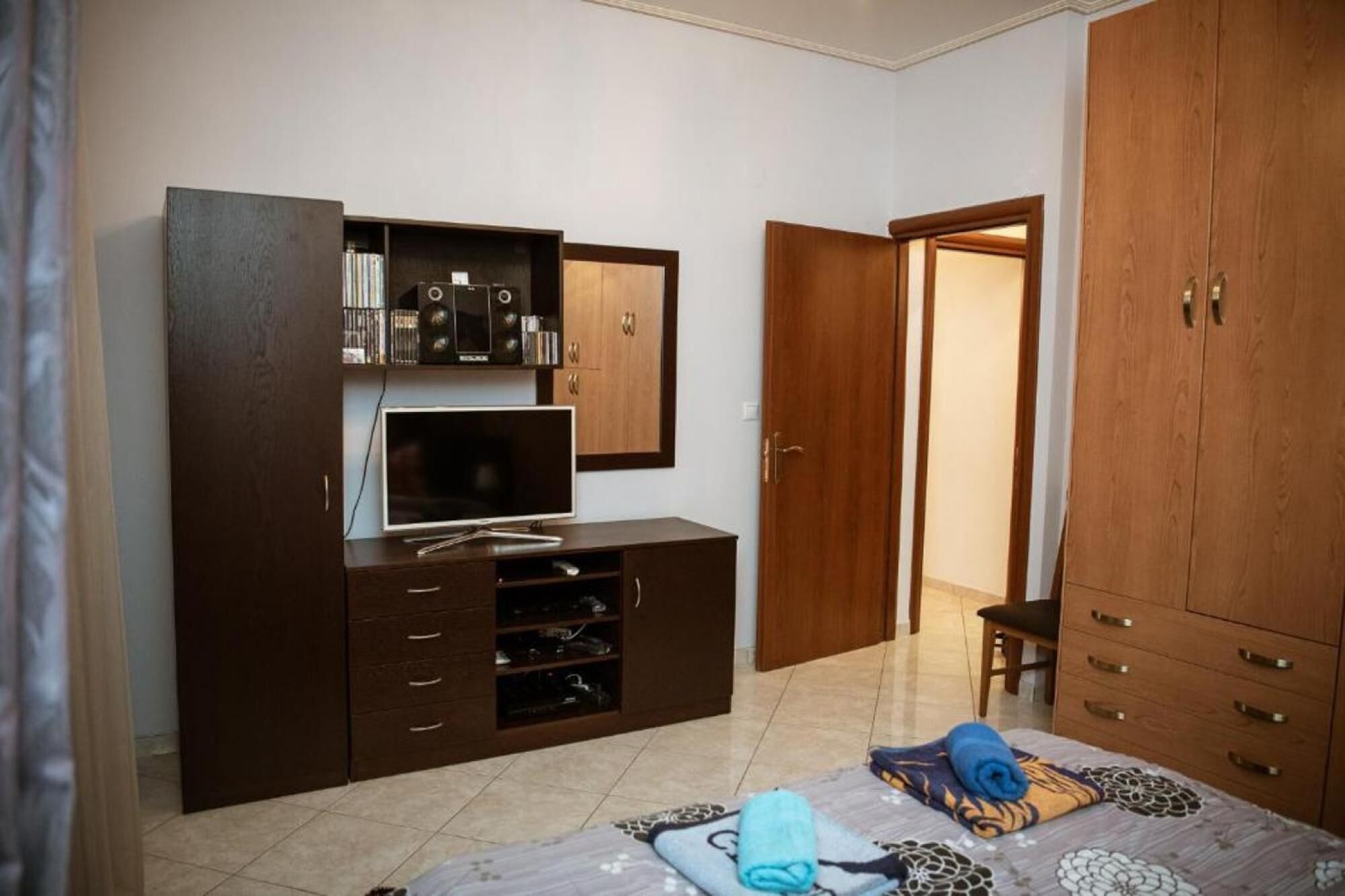 A bedroom with a TV, wooden wardrobe, and a bed with a patterned bedspread.