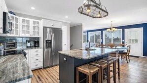 A modern kitchen with white cabinets, a stainless steel refrigerator, a marble countertop, and a central island with bar stools.