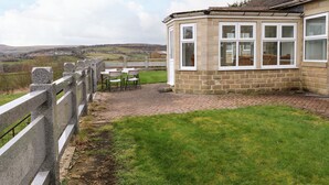 A stone building with a brick patio, a white fence, and a view of the countryside.