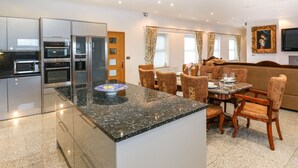 A modern kitchen with built-in appliances and a dining area with a marble island and wooden chairs.