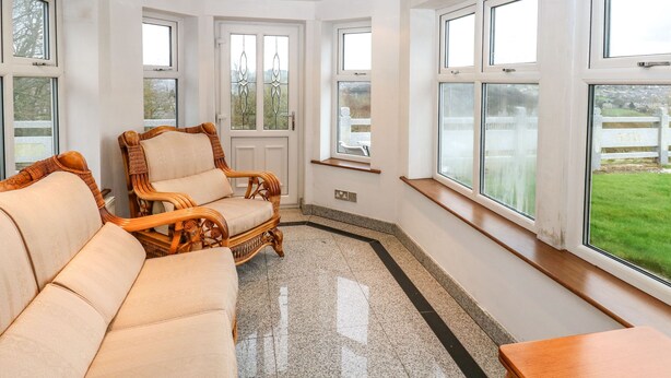 A room with a large window, a wooden table, and two wicker chairs.