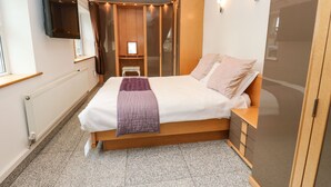 A bedroom with a bed, a bedside table, a wardrobe, a mirror, and a TV mounted on the wall.