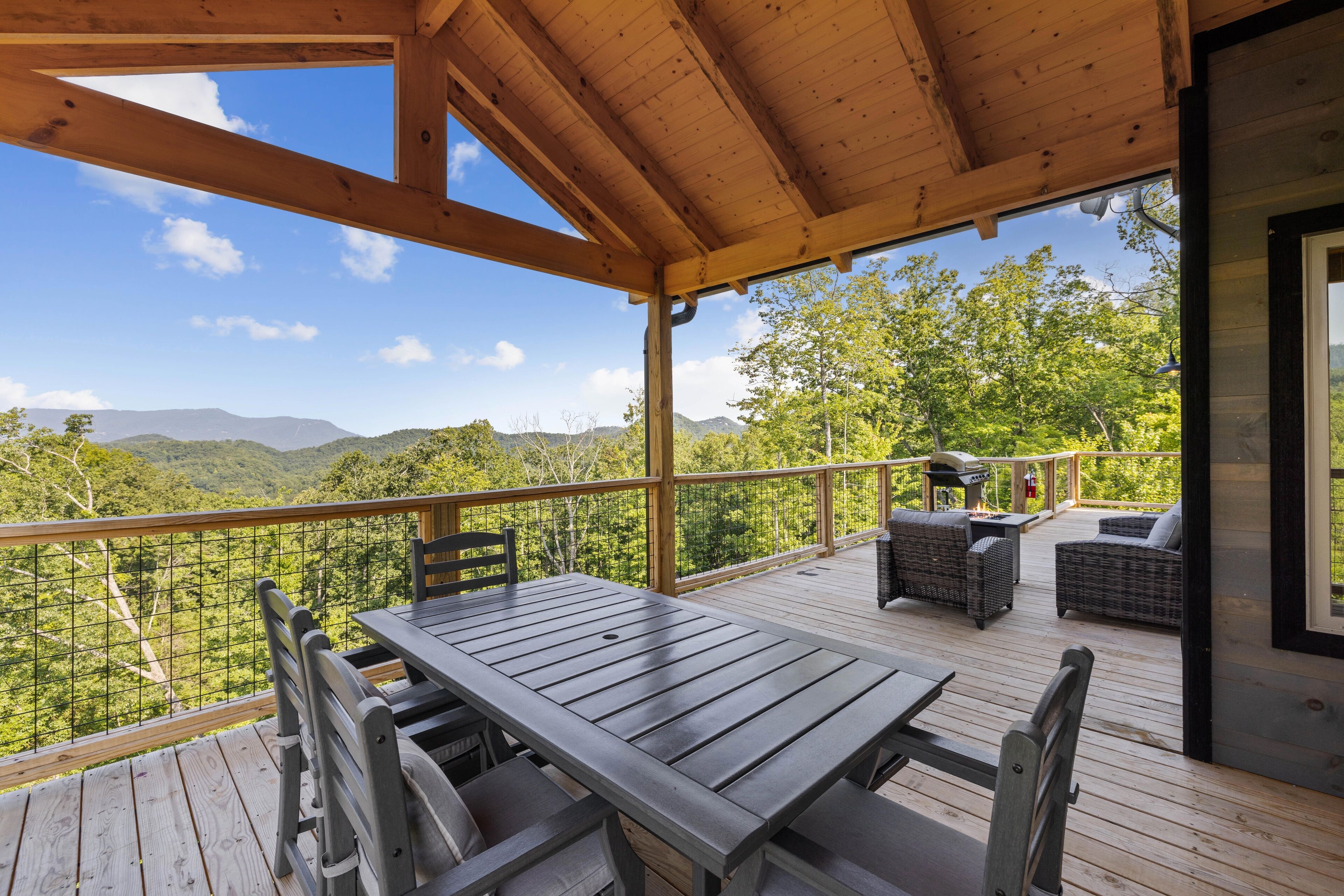 A wooden deck with a table and chairs, overlooking a mountainous landscape.