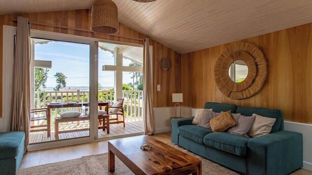 A living room with a wooden ceiling, a green sofa, a wooden coffee table, and a large circular mirror on the wall. - Villa des Sables: Cosy Apartment with Bassin View and Balcony (Lège-Cap-Ferret)