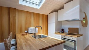 A modern kitchen with wooden cabinetry, a built-in oven, and a skylight. - Villa des Sables: Cosy Apartment with Bassin View and Balcony (Lège-Cap-Ferret)