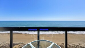 A beach view from a balcony with a glass railing, a clear sky, and a sign indicating a no swimming zone. - Golden Sands 1907 by Seaside Vacations & Sales (Ocean City)