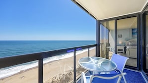 A balcony with a glass table and chairs overlooking a beach. - Golden Sands 1907 by Seaside Vacations & Sales (Ocean City)