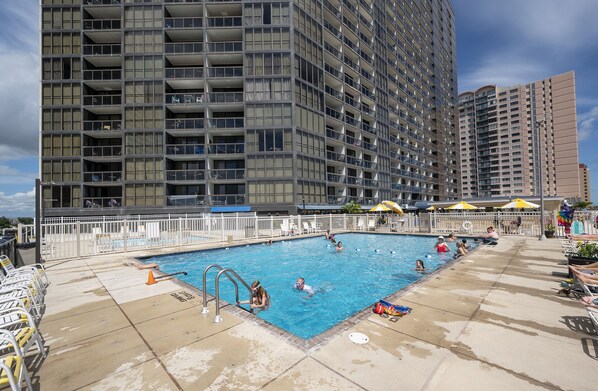 Una piscina rodeada por una cerca blanca, con un edificio alto al fondo.