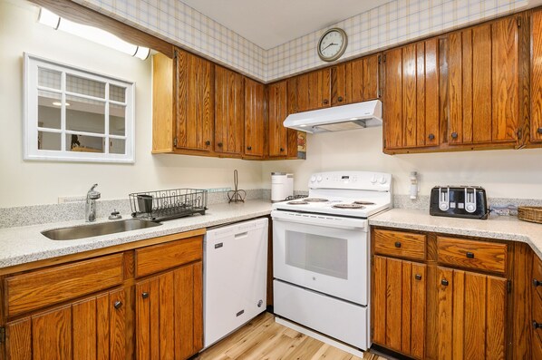 Kitchen features a dishwasher, stove, and toaster, with a window and clock on the wall.