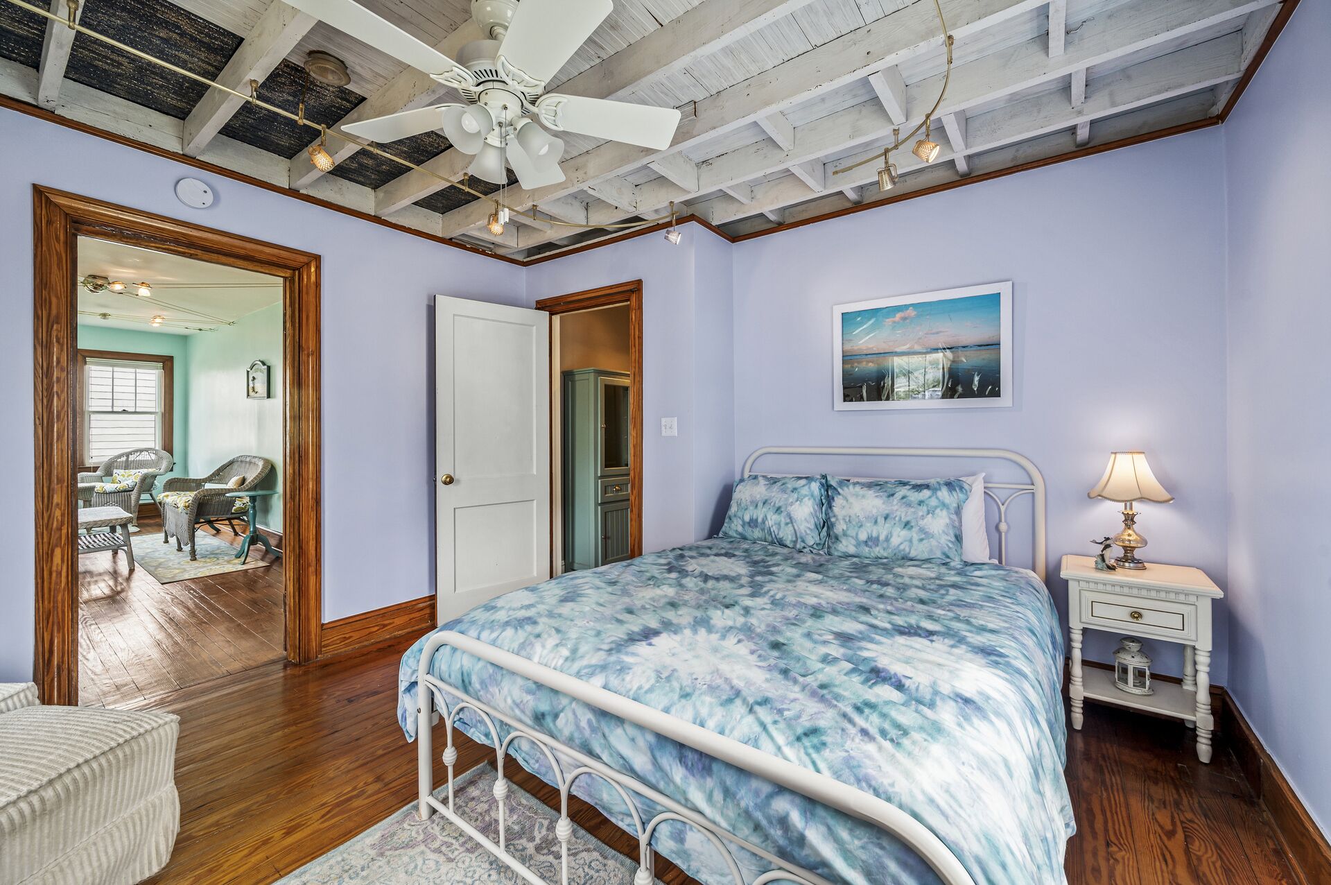 Une chambre à coucher avec un lit, une table de chevet, un ventilateur de plafond et un tableau accroché au mur.