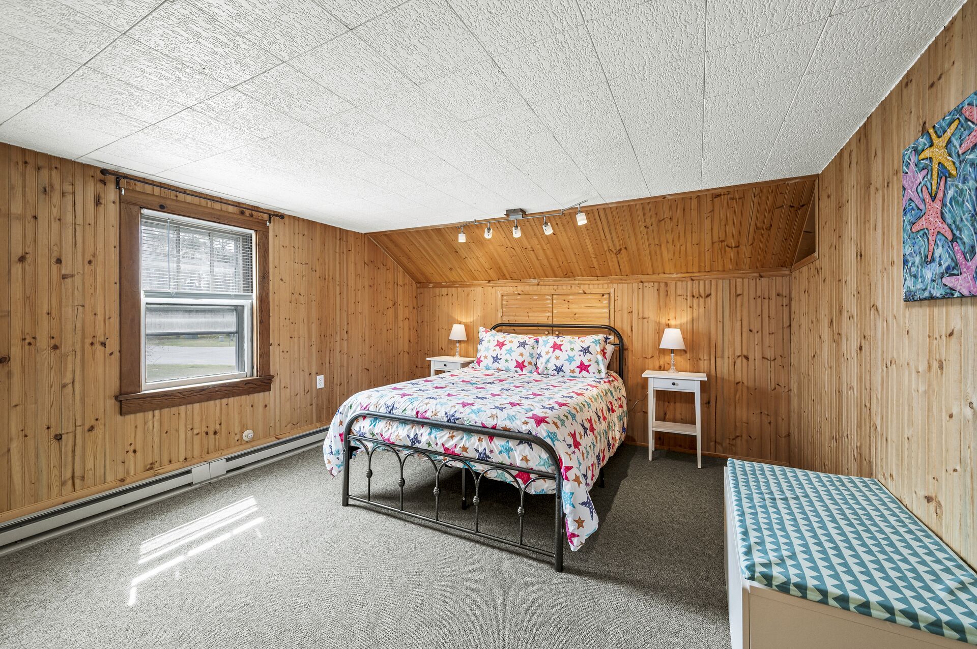 Un dormitorio acogedor con una cama, mesitas de noche, un banco y una ventana.