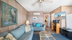 Ein Zimmer mit einer Holzwand, einem blauen Sofa, einem Fernseher und einem Deckenventilator.