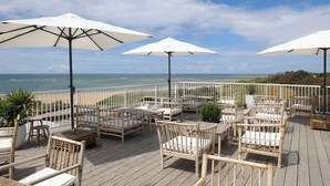A wooden deck with outdoor seating, white umbrellas, and a view of the ocean. - Le Grand Large  (Dolus-d'Oleron)