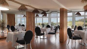 Comedor con mesas dispuestas para seis, paneles de madera y grandes ventanales con vistas al exterior.