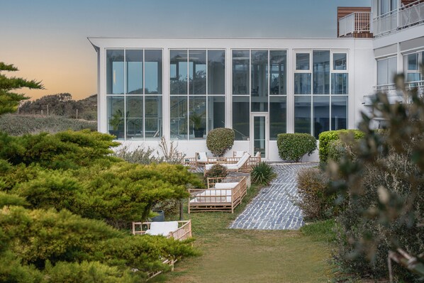 A modern building with large glass windows, a stone pathway, and outdoor seating areas. - Le Grand Large (Dolus-d'Oleron)
