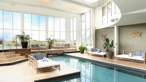 An indoor swimming pool with a sunlit room, large windows, and seating areas with potted plants. - Le Grand Large  (Dolus-d'Oleron)