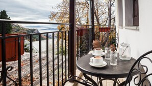 A balcony with a table set for two, overlooking a scenic view of a river and hills. - Maria s Cozy Loft in Makrinitsa (Volos)