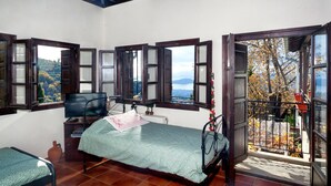 A bedroom with a bed, a desk, a chair, and a television. There are multiple windows with wooden frames and glass panes. - Maria s Cozy Loft in Makrinitsa (Volos)