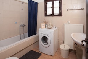 A compact bathroom with a bathtub, a washing machine, a radiator, and a sink. - Maria s Cozy Loft in Makrinitsa (Volos)