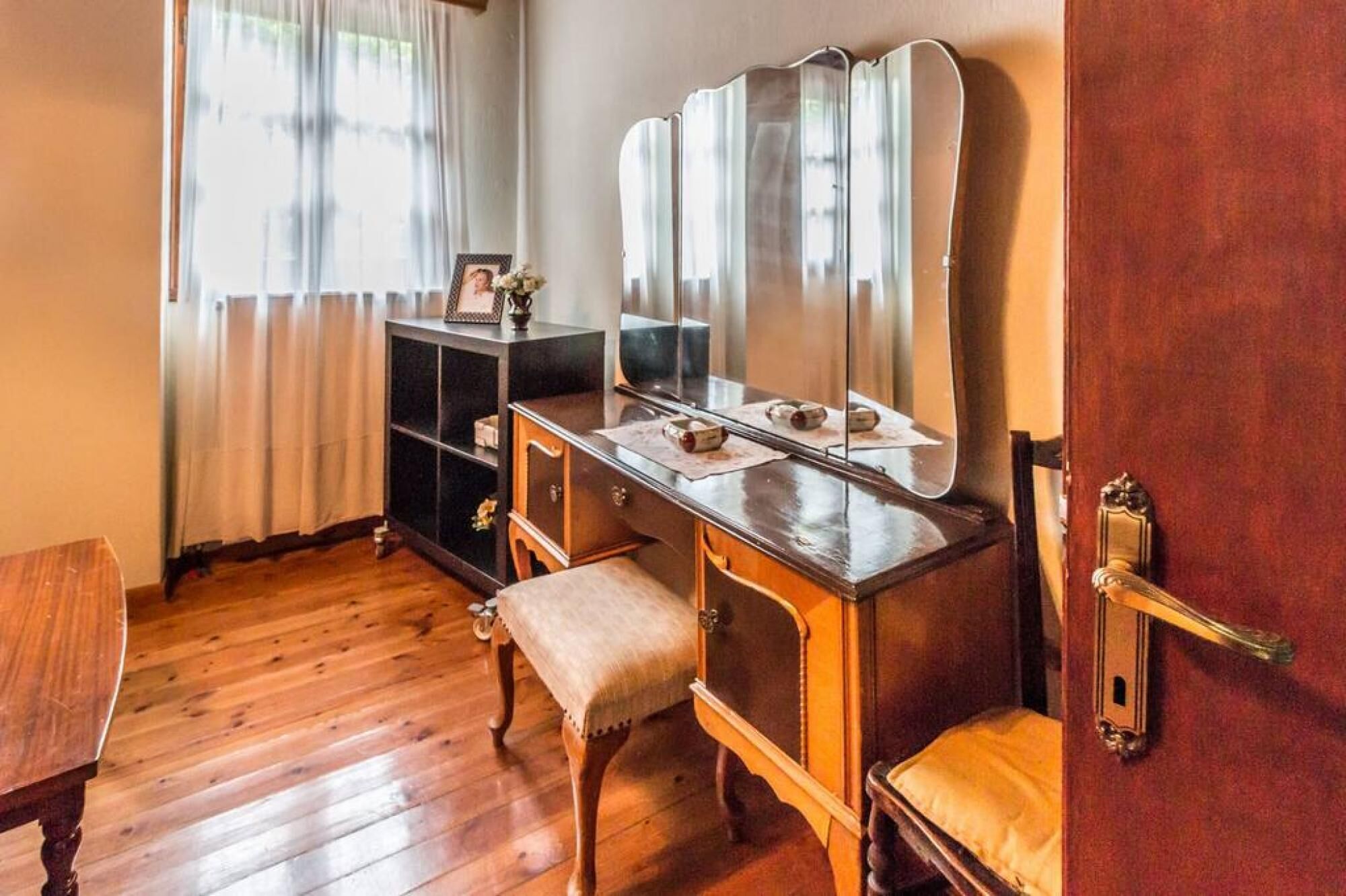 Una habitación con un tocador de madera, un espejo, un banco y una puerta con pomo de latón.