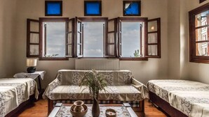 A room with two single beds, a sofa, a table with a vase, and three windows with shutters. - Calliope s Stone Manor (Zagora-Mouresi)