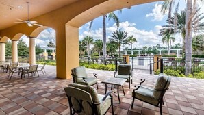 An outdoor patio with seating, a ceiling fan, and a view of palm trees and a pool.