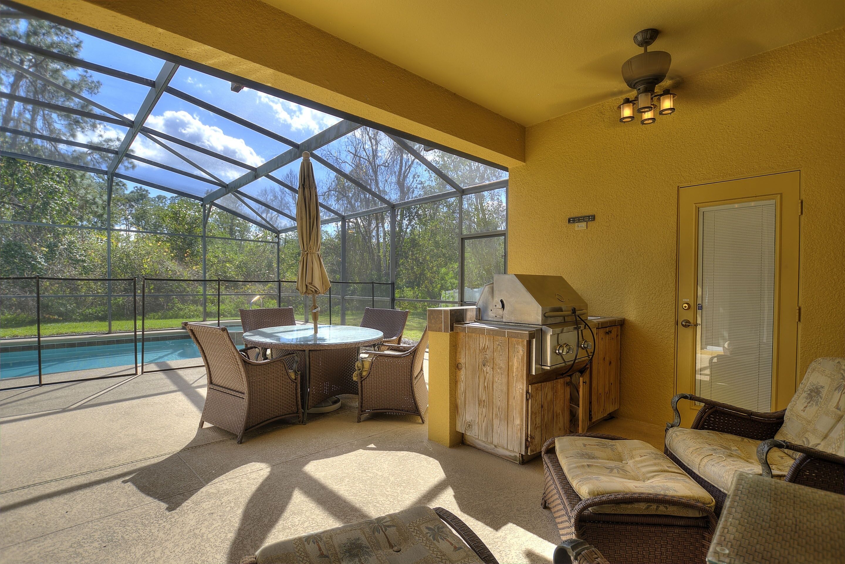 A sunlit patio with a pool, outdoor furniture, and a grill area.