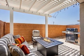 Un patio cubierto con una parrilla, zona de estar y luces colgantes.
