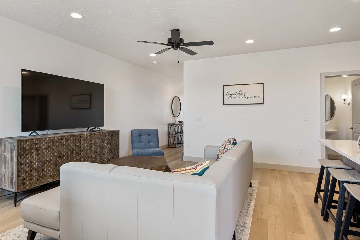 A modern living room with a flat-screen TV, a ceiling fan, and a dining area with a table and chairs.