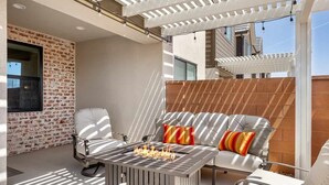 Un área de estar al aire libre con una chimenea, un muro de ladrillo y una pérgola.