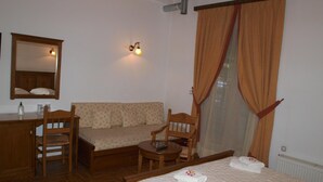 Une chambre d’hôtel comprenant un lit, deux chaises en bois, un canapé, une petite table, un bureau, un miroir et un luminaire fixé au mur.