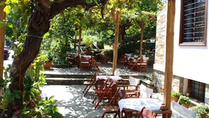 Une terrasse extérieure avec des tables et des chaises en bois, entourée de verdure et d’un mur de pierre.