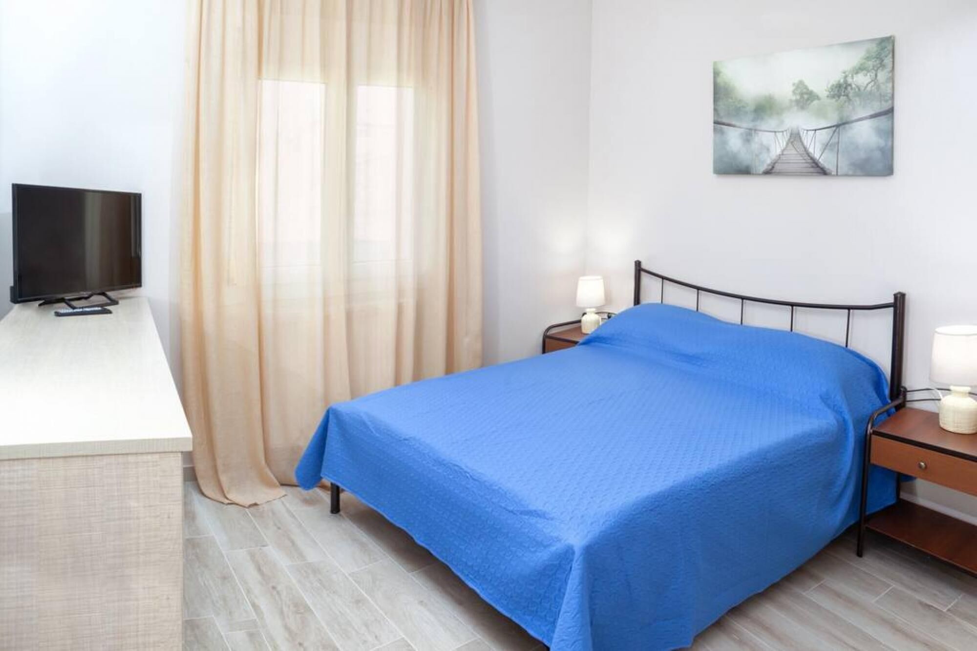 A bedroom with a bed, a TV, a nightstand, a lamp, and a painting on the wall.