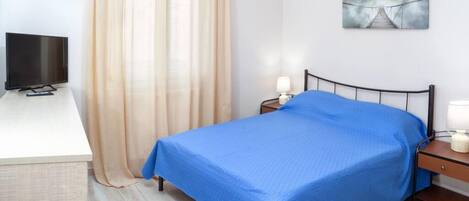 A bedroom with a bed, a TV, a nightstand, a lamp, and a painting on the wall.
