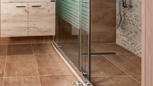 A modern bathroom with a glass shower enclosure, a wooden vanity, and patterned tiles. - Aethra House in Agria Volou (Volos)