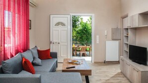 A living room with a grey sofa, red cushions, a coffee table, and a TV on a wooden cabinet. - Aethra House in Agria Volou (Volos)