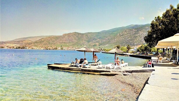 A clear waterfront with a dock, lounge chairs, and umbrellas. - Aethra House in Agria Volou (Volos)