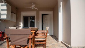 An outdoor patio with a wooden table and chairs, a ceiling fan, and a view of the house.
